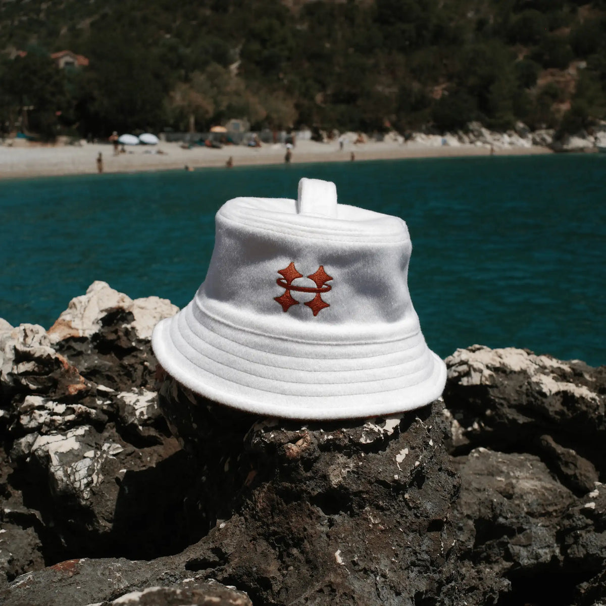 White Halo sauna hat with a logo on rocks by a beach