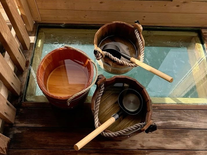 Three sauna buckets placed on the floor of wood sauna with glass panel