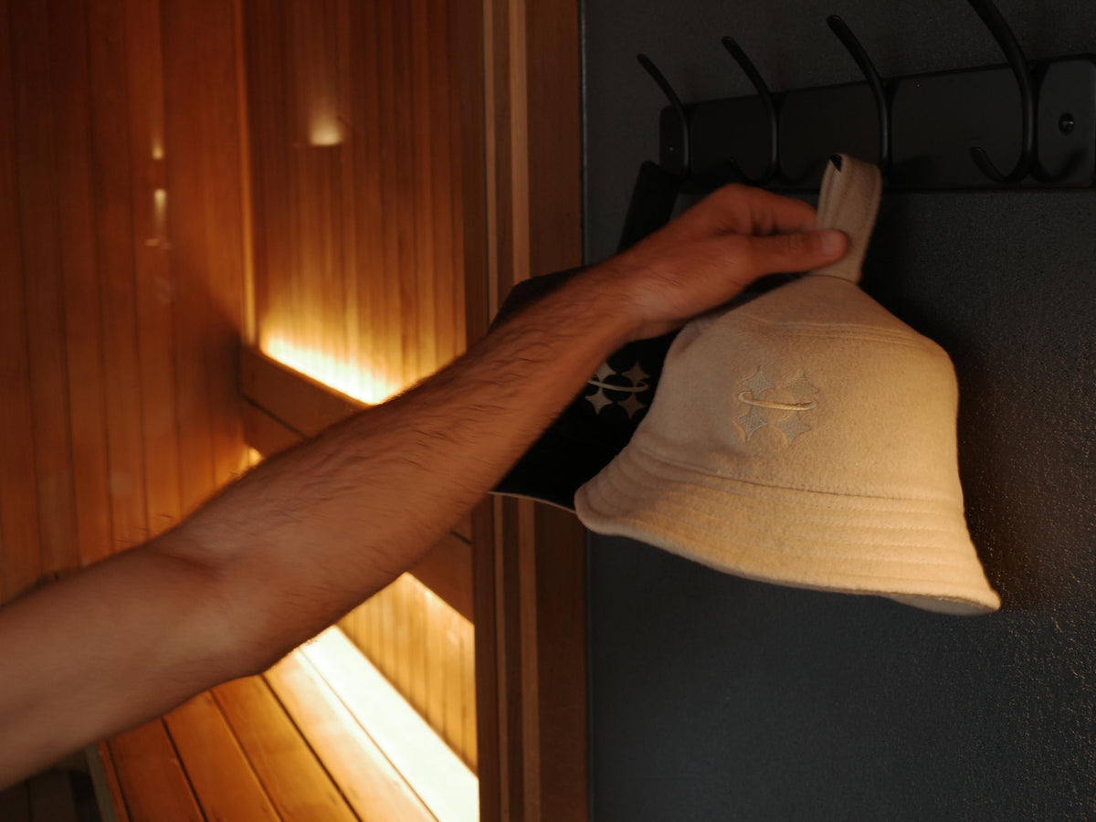 Arm reaching for a hanging Halo sauna hat next to the sauna