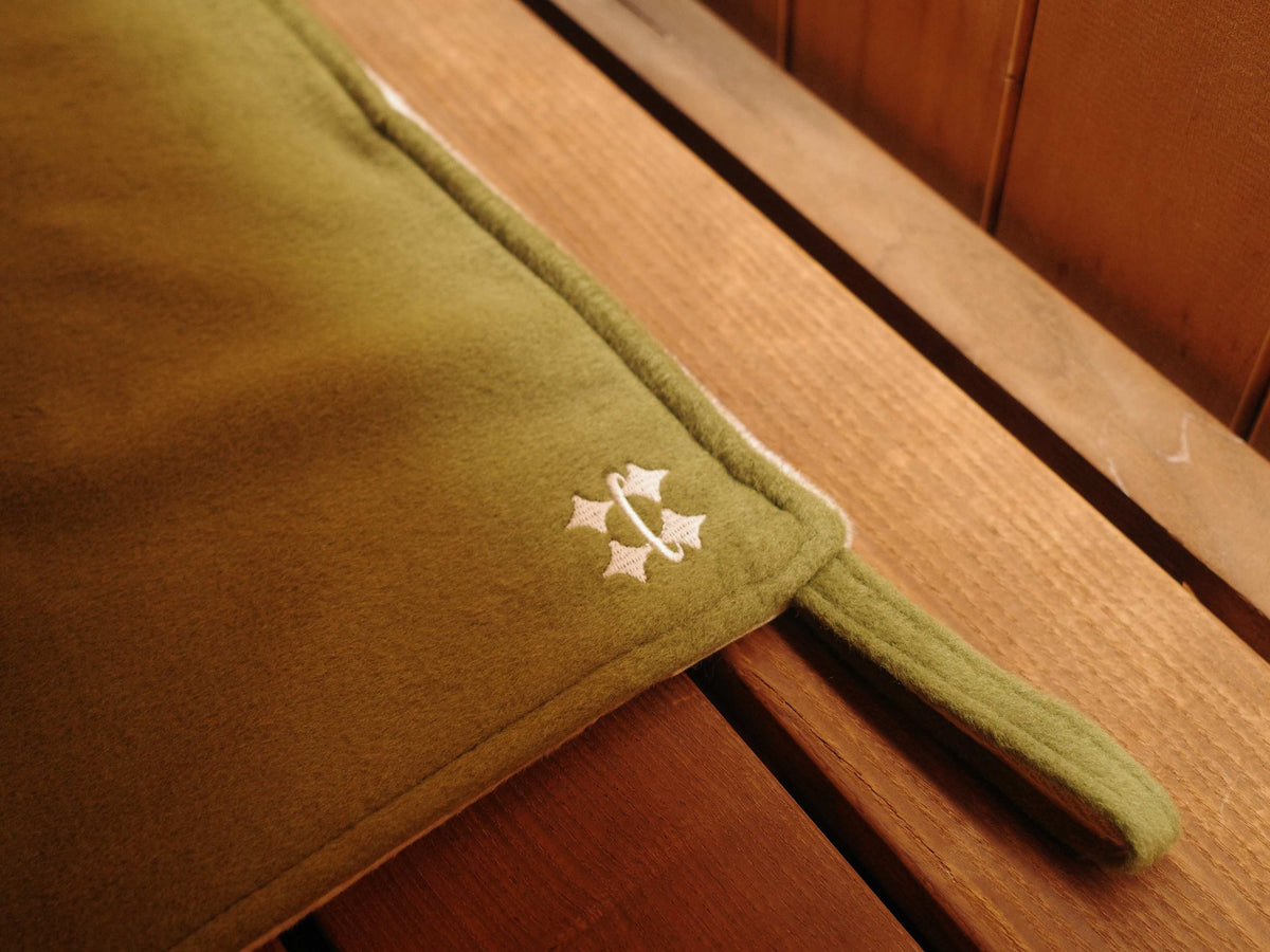 Olive green Halo sauna mat placed on a wooden bench