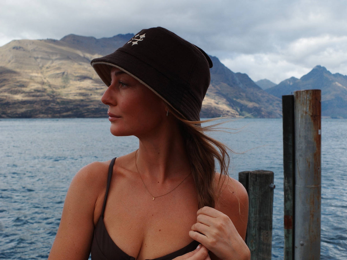 Woman holding her hair wearing a brown Halo sauna hat next to a large body of water.