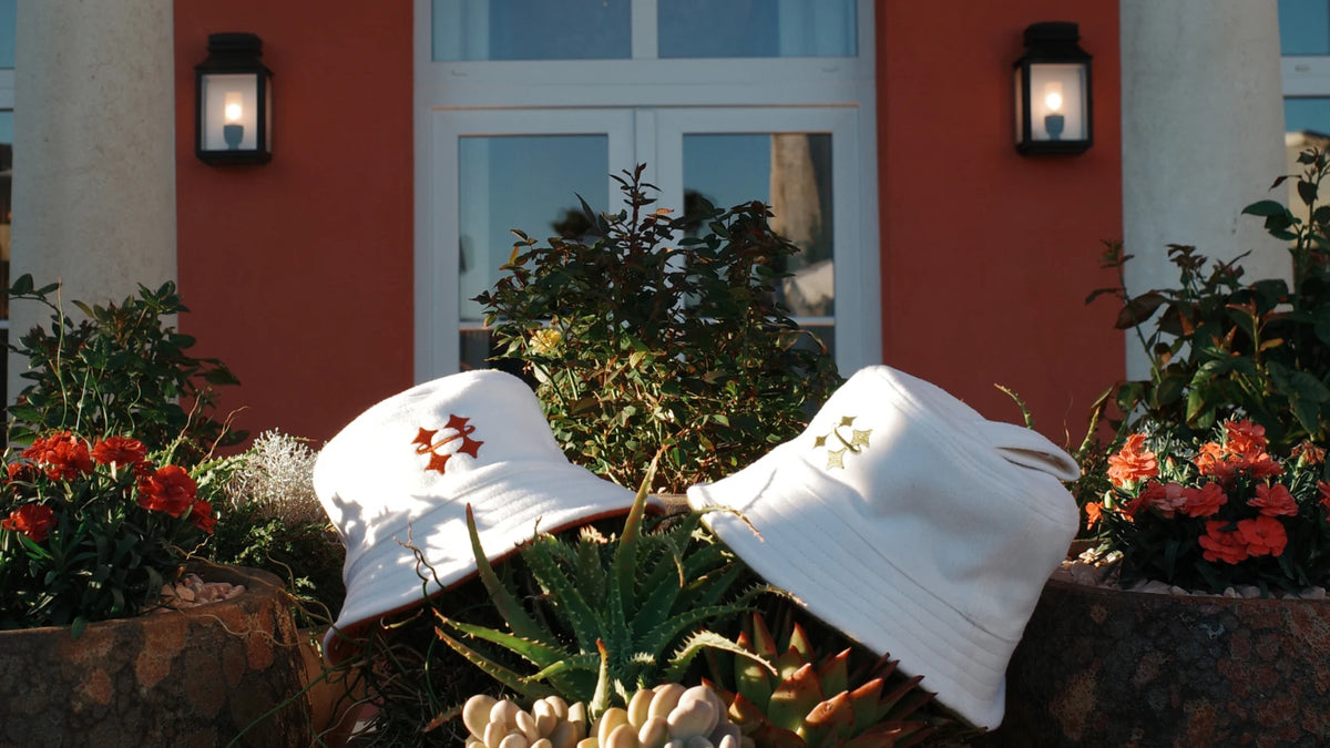 Two white Halo sauna hats with embroidered logos resting in a terracotta planter alongside succulents, set against a red stucco building facade with lit wall lanterns.